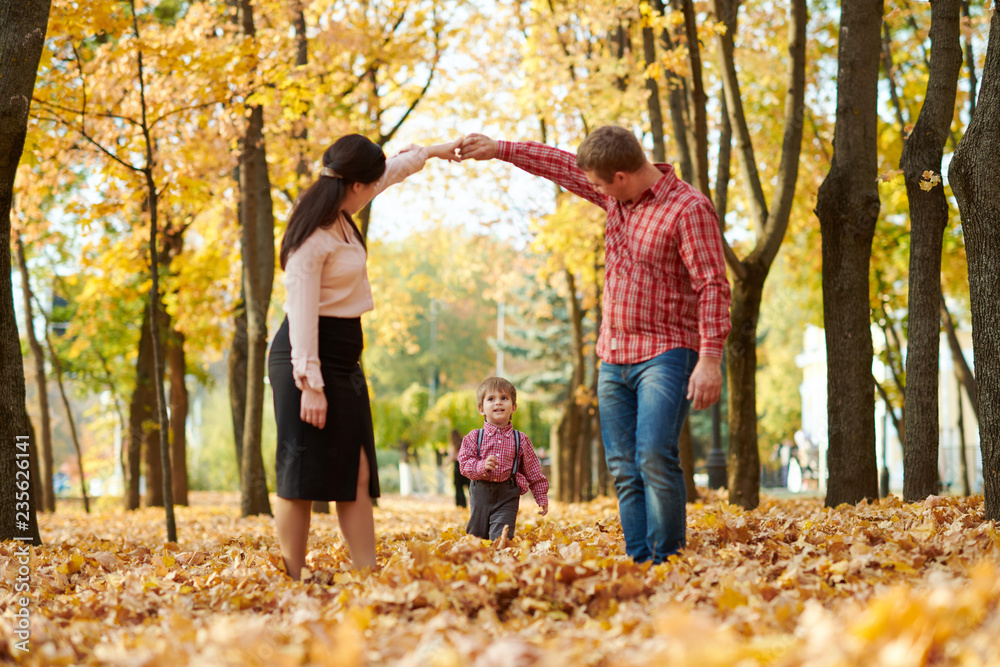 Parents and child are walking in autumn city park. Bright yellow trees.