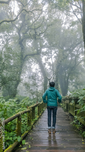 Grain and Noise of fog in forest is man Wear a green sweater, hood and jeans. Brown leather boots on a wooden walkway in the cold, alone hiking.