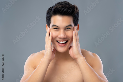 Portrait of handsome smiling young Asian man with hands touching face