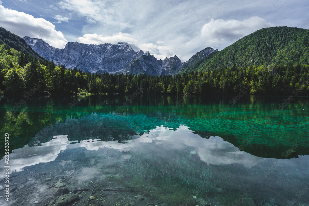 View of a mountain lake Lago Fusine, Julian alps and Tirol. Beautiful and clear alpine lake with blue and green colors, deep forest and high alpine peaks and rock faces.