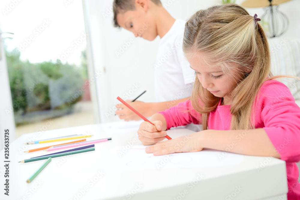 two beautiful young kids boy and girl drawing on a white paper with color pencil