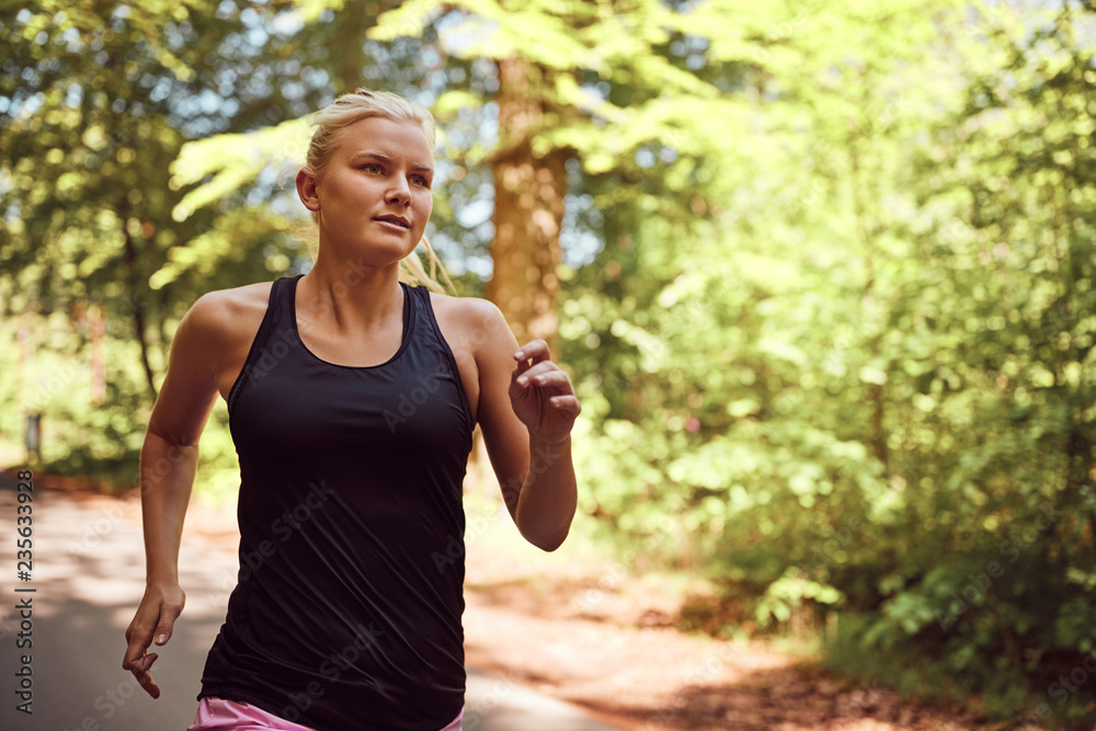 Sporty young blonde woman running alone on a forest path Sporty young blonde woman running alone on a forest path