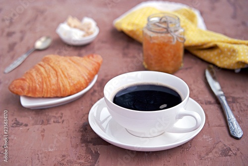 Breakfast: a cup of coffee, fresh croissant and orange jam