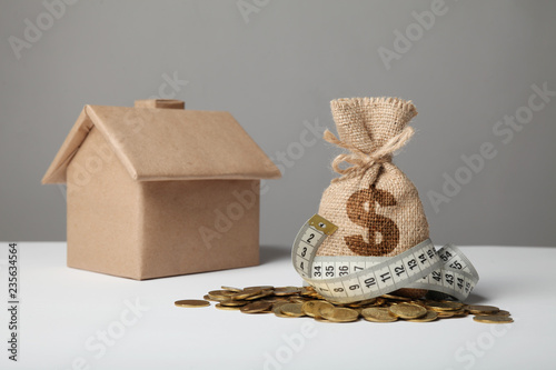 Crafting bag with dollar logo on yellow coins and measuring tape on background of figure of house. Сoncept of saving money when buying or renting housing.