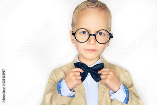 Cute boy wearing a suit and glasses adjusting his bowtie