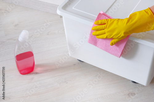 Cleaning concept. Hand in yellow rubber protective glove wipes white box with pink cleaner at room. Maid or housewife cares about house.