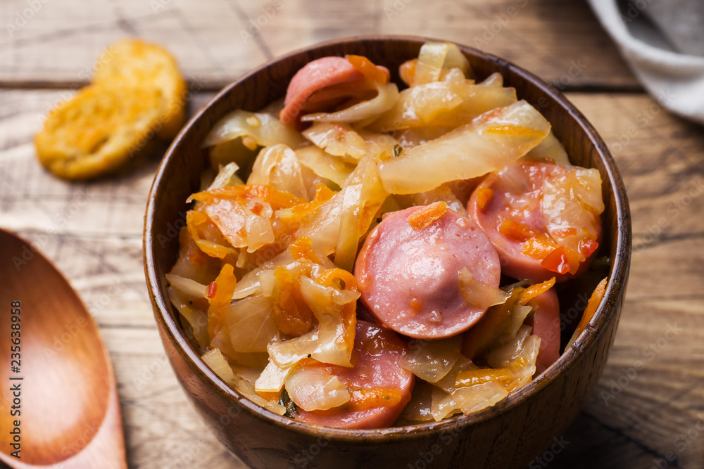 Stewed cabbage with sausages in wooden bowls on the table. Selective focus. Stewed cabbage with sausages in wooden bowls on the table. Selective focus.