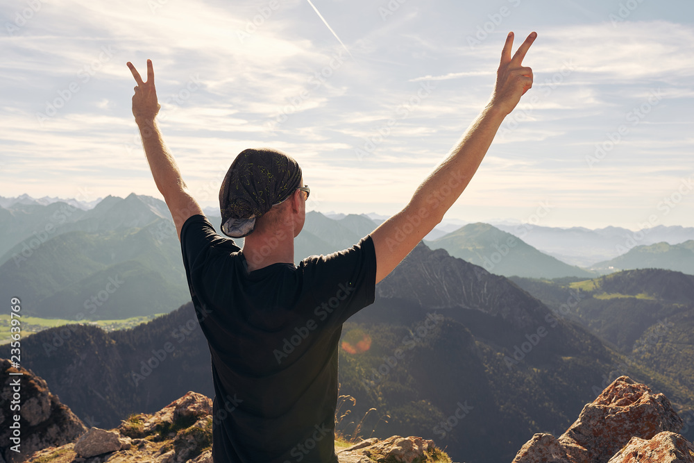 Mann von hinten steht auf einem Gipfel in Siegerpose und schaut auf deie Berge Mann von hinten steht auf einem Gipfel in Siegerpose und schaut auf deie Berge