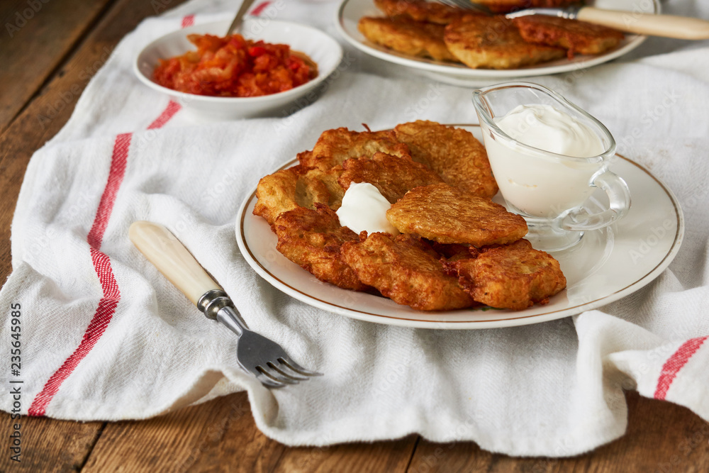 Potato fritters with sour cream and tomato sauce on a wooden table Potato fritters with sour cream and tomato sauce on a wooden table