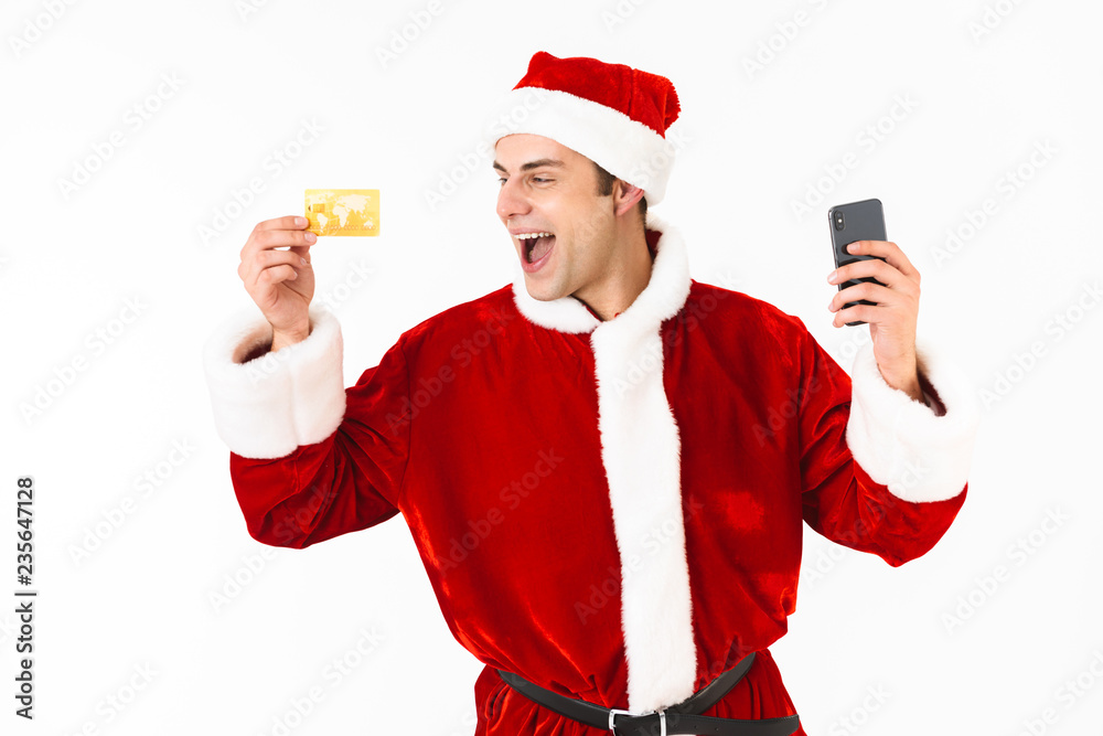 Image of optimistic man 30s in santa claus costume holding cell phone and credit card, isolated on white background in studio Image of optimistic man 30s in santa claus costume holding cell phone and credit card, isolated on white background in studio