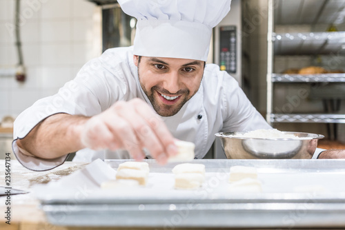 Foto Handsome baker smiling and laying uncooked dough on tray