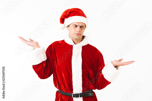 Portrait of european man 30s in santa claus costume and red hat holding copyspace at palm, isolated over white background in studio