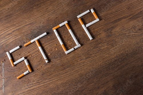 Creative background, the word stop is made up of cigarettes on a brown wooden background. The concept of smoking kills nicotine poisons. Copy space.