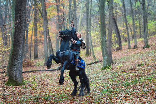 Viking warrior man riding horse in forest holding sword attacking