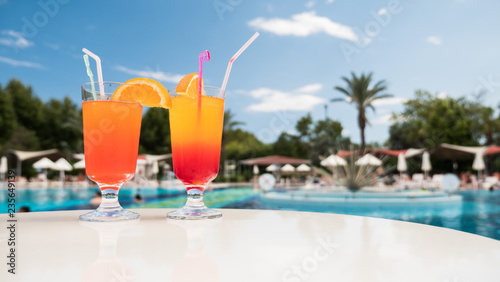 Two cocktails are on the table against the background of the pool. Holiday at the resort with swimming pool