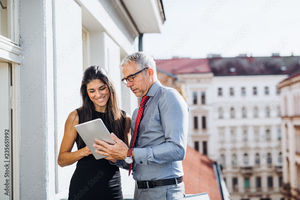 Man and woman business partners with tablet standing on a terrace in city, talking.