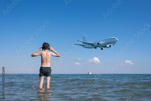 Teen boy on the beach under the landing planes. Traveling on an airplane with children. Concept © flowertiare