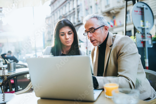 Man and woman business partners with laptop sitting in a cafe in city, talking.