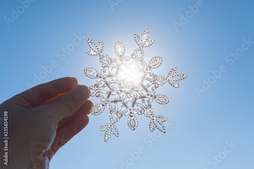 Female hand with sparkling huge snowflake on the sky background. Concept of Winter and Christmas vacation on the beach and resort.