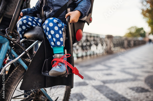 A small toddler boy sitting in bicycle seat outdoors in city. Copy space.