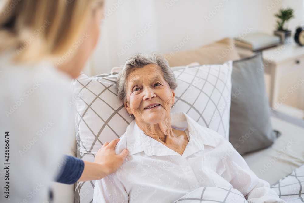 A health visitor talking to a sick senior woman lying in bed at home. - obrazy, fototapety, plakaty 