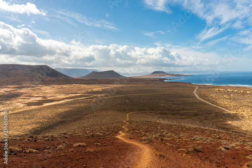 Desert landscape with a long dirt road leading towards volcano craters and the ocean. La Graciosa   Canary Islands  Spain.