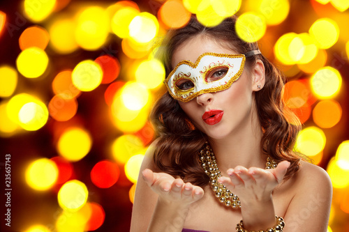 Beauty model woman wearing venetian masquerade carnival mask at party over holiday dark background with magic glow. Christmas and New Year celebration. Glamour lady with perfect make up and hairstyle