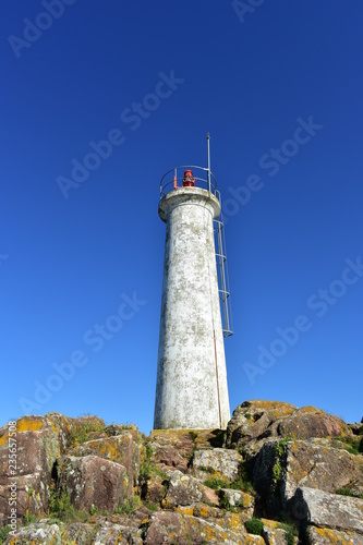 Old white lighthouse on the rocks with lightning rod. Blue sky, sunny day. Galicia, Spain.