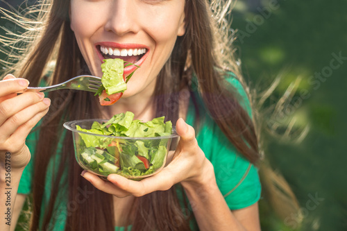 Beautiful caucasian woman eating salad over green natural background	