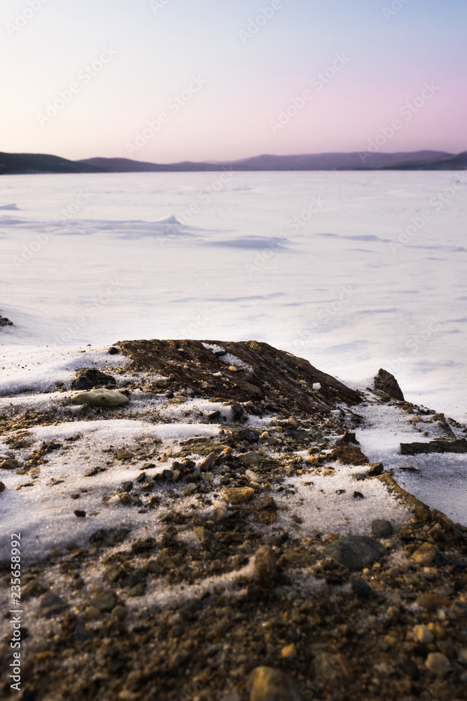 A beautiful view from the coast to the freezing lake against the backdrop of a gloomy sky with sunset. Winter snow covered lake Turgoyak. Landscape. A beautiful view from the coast to the freezing lake against the backdrop of a gloomy sky with sunset. Winter snow covered lake Turgoyak. Landscape.