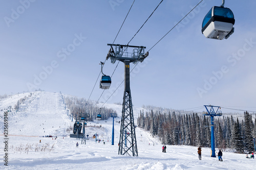 Ski lift, cable car funicular with open cabin on the background of valley, skiers, snowboarders, snow-capped mountains, evergreen trees. Concept Alps resort, Georgia, Sochi, Matterhorn