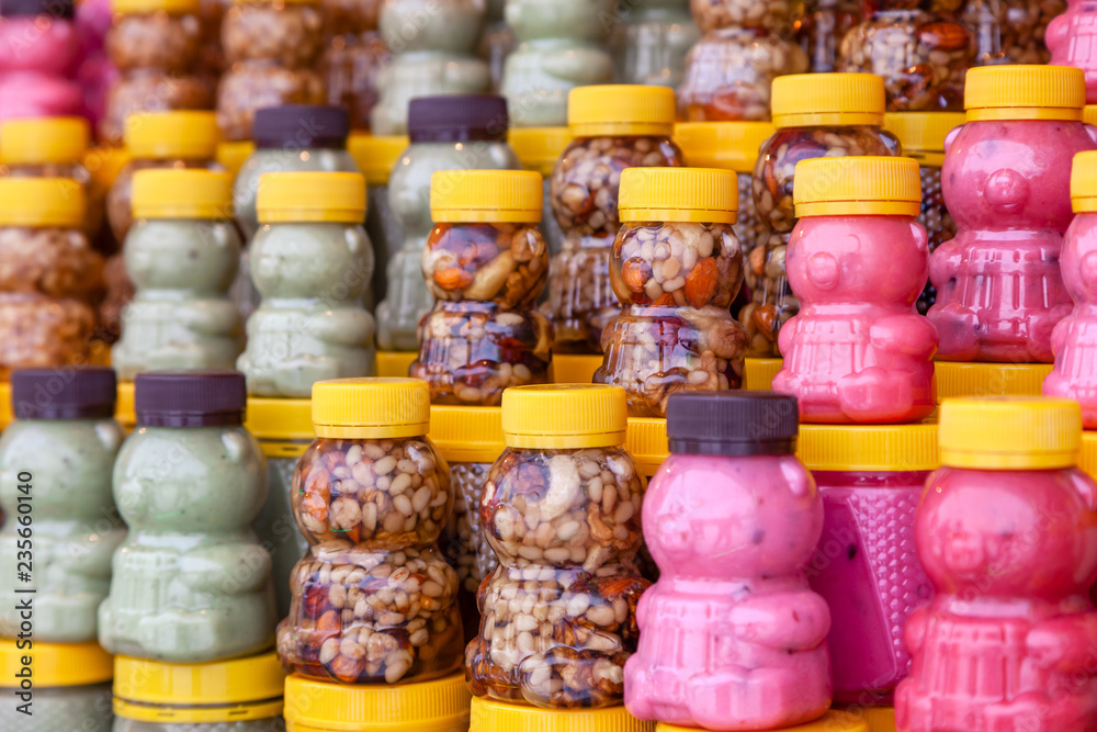 Fototapeta premium Many transparent plastic jars with yellow lids in the shape of a bear with green, pink honey mixed with nuts. Concept of local Siberian delicacies and specialties