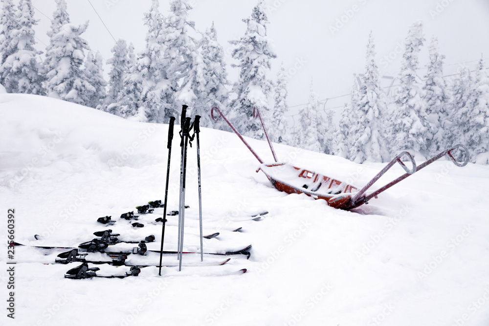 Skis with bindings, ski poles and an empty cradle for transporting people and products to the mountain covered with snow at ski resort. Concept ambulance, rescue, injury