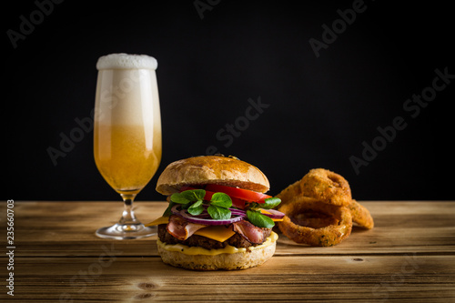 Burger mit Zwiebelringe und Bier auf Holz und schwarzer Hintergrund