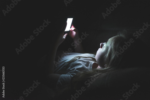 Tableau sur toile Depressed girl lying down on a couch in the dark while using her smartphone