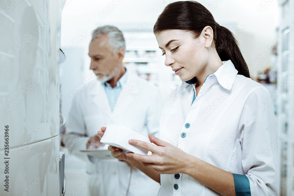 Obraz premium Attentive young assistant checking expire date of pills