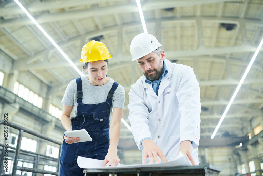 Portrait of female factory worker looking at plans with mature engineer in workshop, copy space Portrait of female factory worker looking at plans with mature engineer in workshop, copy space