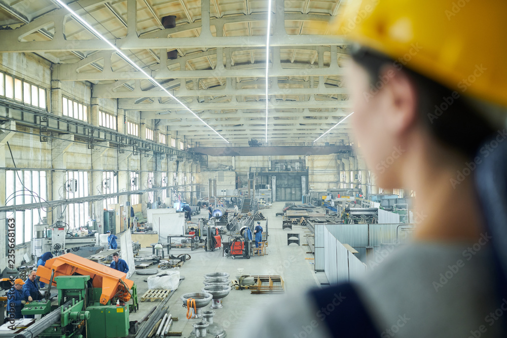 Naklejka premium Back view portrait of unrecognizable female worker looking at interior of factory workshop from above, copy space