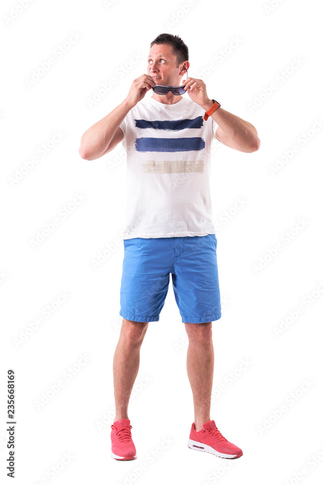 Casual young adult man in summer clothes removing sunglasses looking up in disbelief. Full body isolated on white background. Casual young adult man in summer clothes removing sunglasses looking up in disbelief. Full body isolated on white background.