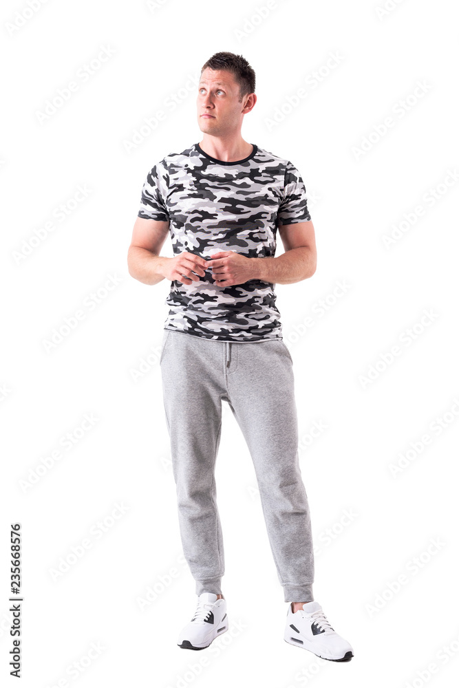 Fototapeta premium Young adult man in sporty clothes and army t-shirt looking up and thinking. Full body isolated on white background. 