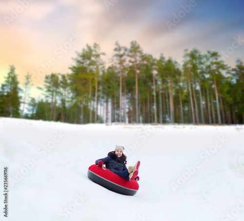 winter, leisure and entertainment concept - happy teenage girl sliding down hill on snow tube