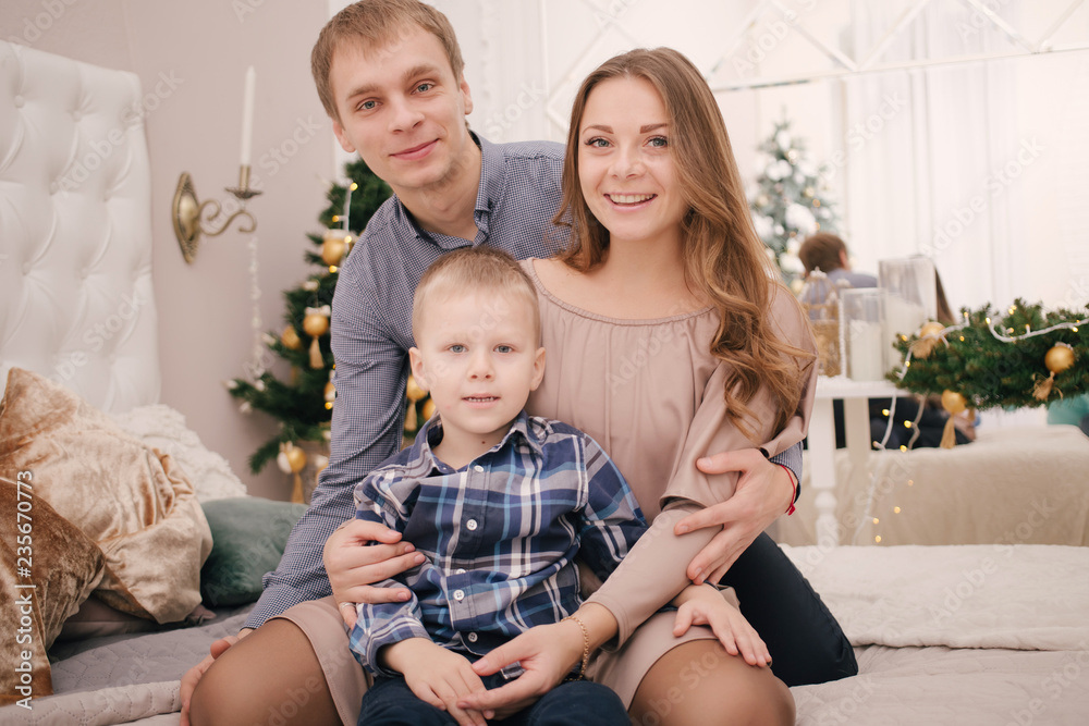Happy family Mom, Dad and son in light bedroom near the Christmas tree decorated for xmas. Parents with a child celebrate the holiday. Merry Christmas and Happy New Year 2019 Holidays concept