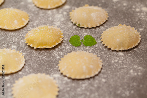 Tasty raw ravioli with flour on dark background. Process of making italian ravioli.