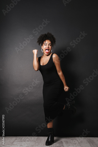 Full length photo of gorgeous afro american woman wearing black dress standing, isolated over dark background