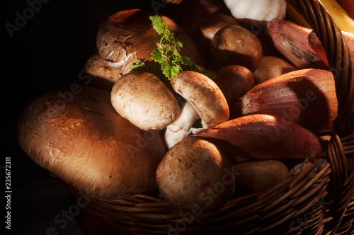 Close up of mushrooms and shallots in a wicker basket with a sprig of parsley in warm lighting