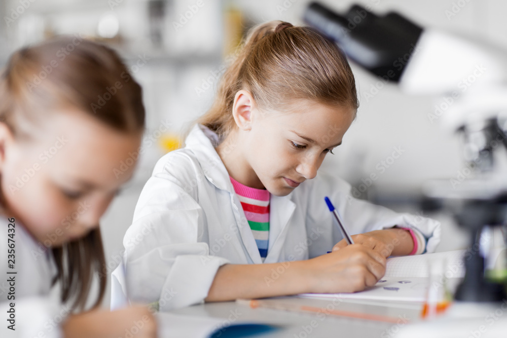 education, science and children concept - kids studying chemistry at school laboratory and writing to workbooks education, science and children concept - kids studying chemistry at school laboratory and writing to workbooks