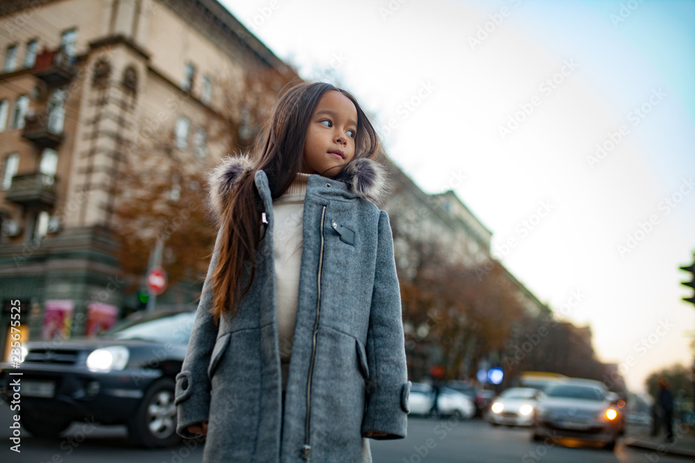 Child girl is standing at the sidewalk on background of city street in evening. Child girl is standing at the sidewalk on background of city street in evening.