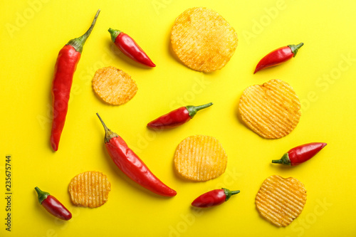 Tasty potato chips with chili pepper on color background