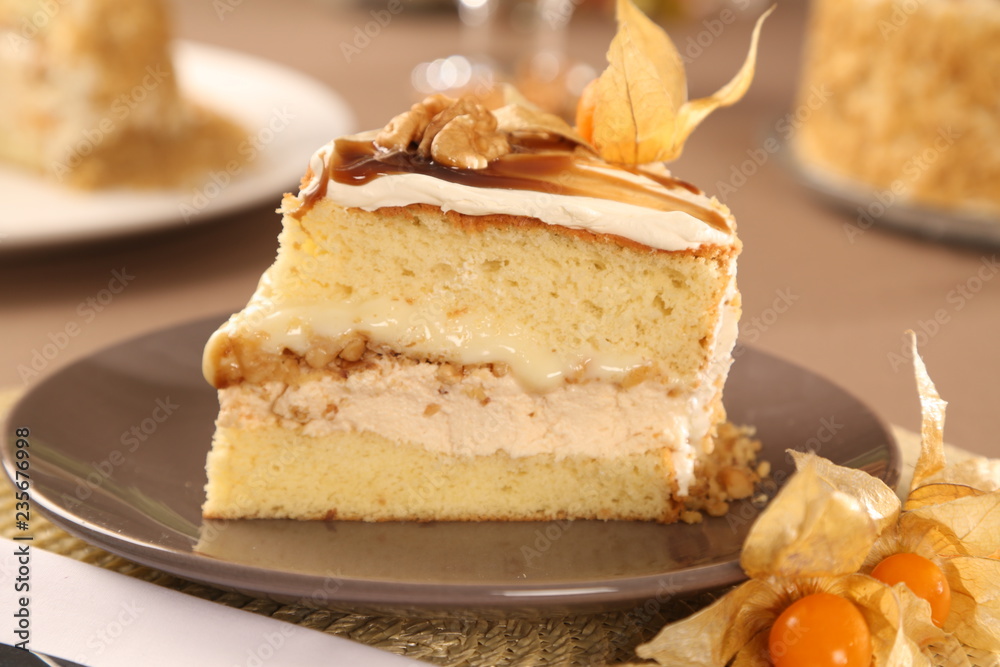 Macro close up of appetizing slice of white chocolate cake with nut and Physalis with out of focus cake in background. Macro close up of appetizing slice of white chocolate cake with nut and Physalis with out of focus cake in background.