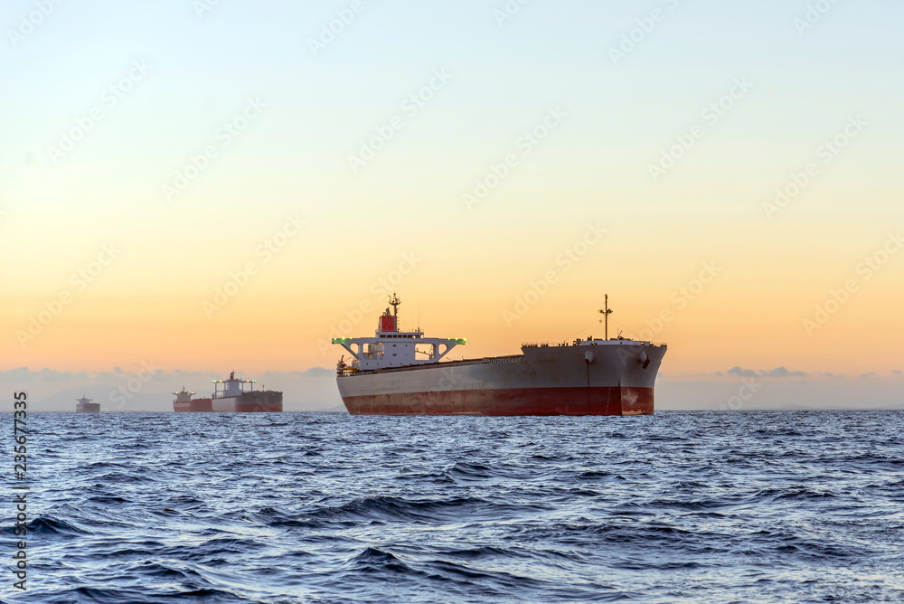 huge ships at sea at sunset with orange sky bacjground